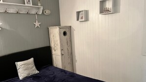 Ein Schlafzimmer mit Bett, Kleiderschrank und Regalen an der Wand mit dekorativen Gegenständen.