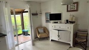 Ein Zimmer mit Fernseher, einem Sessel, einem Schrank und Blick ins Freie.