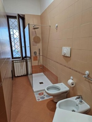 Baño compacto con ducha, inodoro, bidé y una pequeña ventana.