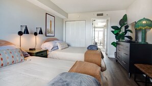 A bedroom with two beds, a dresser, a bench, and a door leading to a balcony.