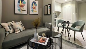 A modern living room with a sofa, a coffee table, and a dining area with chairs. There are framed artworks on the wall and a kitchen in the background. - Relax in Style Central 1BDR Cityscape (Dubai)