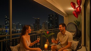 A couple seated on a balcony with a city view, holding wine glasses, and a candle on a small table. - Relax in Style Central 1BDR Cityscape (Dubai)