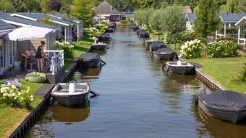 A canal with boats docked on both sides, surrounded by houses with sloped roofs and a grassy area with flowers.