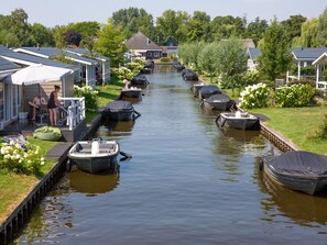 A canal with boats docked on both sides, surrounded by houses with sloped roofs and a grassy area with flowers. - Nice Chalet With ac and Sloop (Giethoorn)