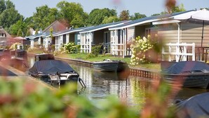 A canal with boats and a row of houses with a covered walkway. - Nice Chalet With ac and Sloop (Giethoorn)