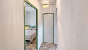 A narrow hallway with a stone-patterned floor, a bed with white bedding, and a green-framed mirror reflecting a room with a wicker light fixture. - Gorgeous home in Lege-Cap-Ferret with WiFi (Lege-Cap-Ferret)