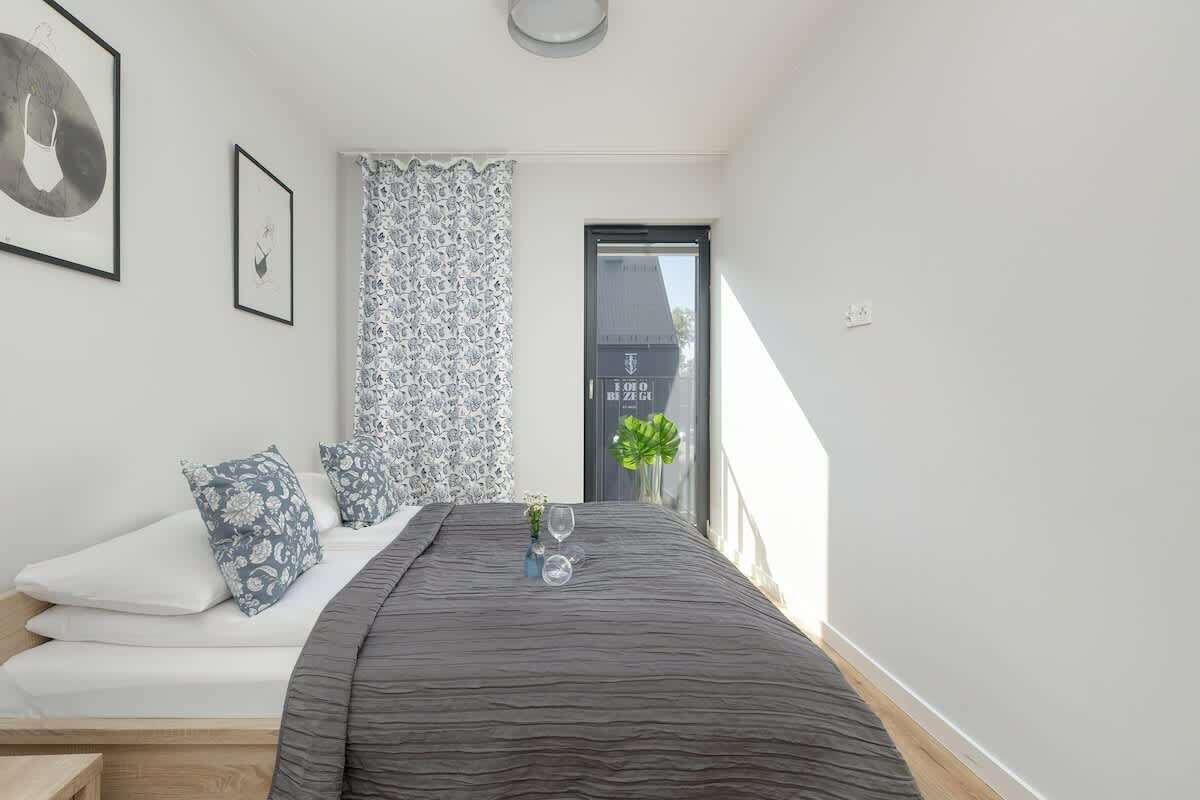 A bedroom with a bed, pillows, a bedside table, a window with a view, and a door.