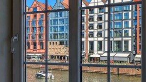 A window with a view of a river, buildings, and a boat.