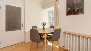 A dining area with a round table, four chairs, a vase with flowers, a radiator, and a door with a frosted glass panel.