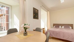A modern hotel room with a round dining table, a bed with a pink quilt, and a painting on the wall.