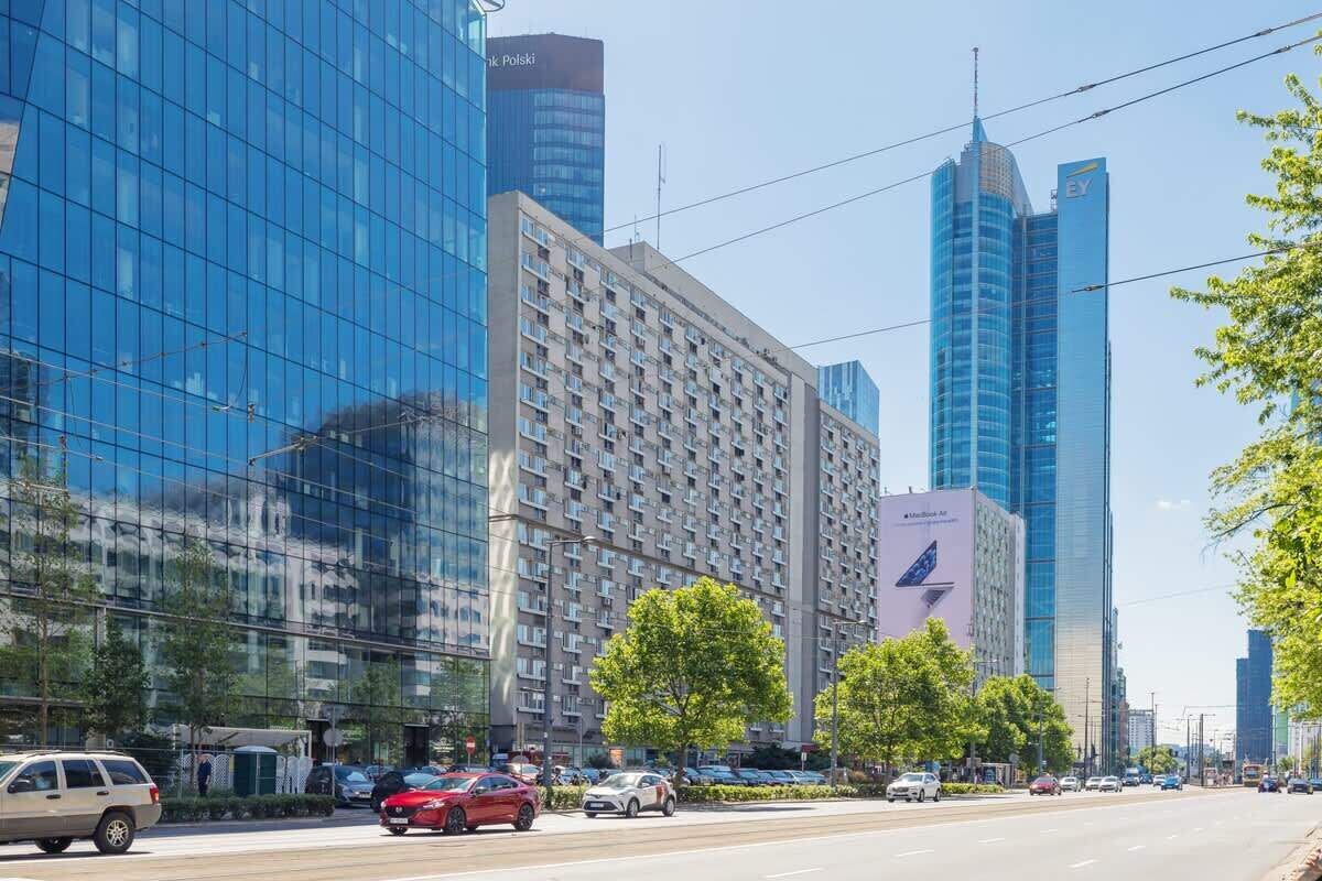 A modern urban street with high-rise buildings, including a prominent glass skyscraper and a hotel with a visible logo.
