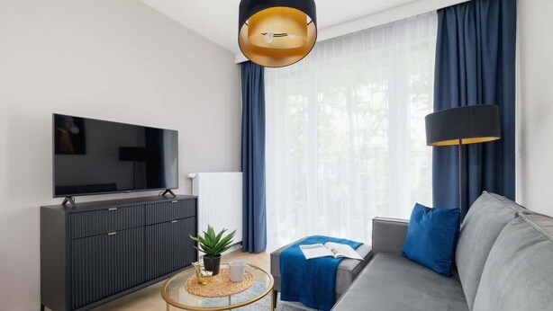 Una sala de estar moderna con televisor de pantalla plana, sofá gris oscuro, cortinas azules y una mesa de centro redonda.