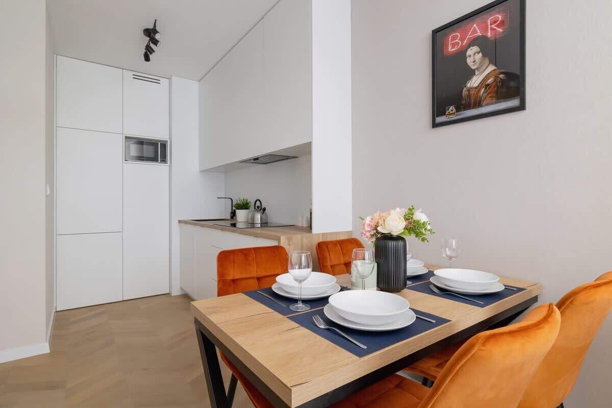 Et moderne spiseområde med et træbord dækket til fire personer, orange stole og en vase med blomster.