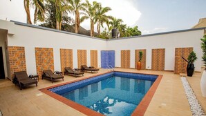 A swimming pool with lounge chairs, a water feature, and palm trees in the background. - Stay And Homely Quintessential Hotel (Abuja)