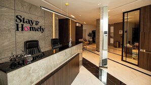 A modern hotel reception area with a marble counter, two black chairs, and a sign that reads "Stay & Homely". - Stay And Homely Quintessential Hotel (Abuja)
