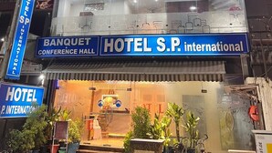 Un hotel de varios pisos con fachada de vidrio, señalización para un salón de banquetes y conferencias, y una entrada visible con plantas en macetas.