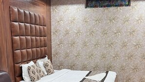 Habitación de hotel con cama, una mesita de vidrio, un sillón de cuero, piso de madera y ventilador de techo.