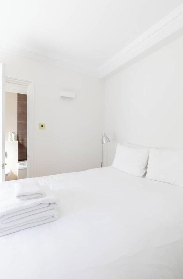 A hotel room with a neatly made bed, a bedside lamp, and a door leading to a bathroom.