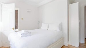 Habitación blanca con cama, una puerta y una lámpara.