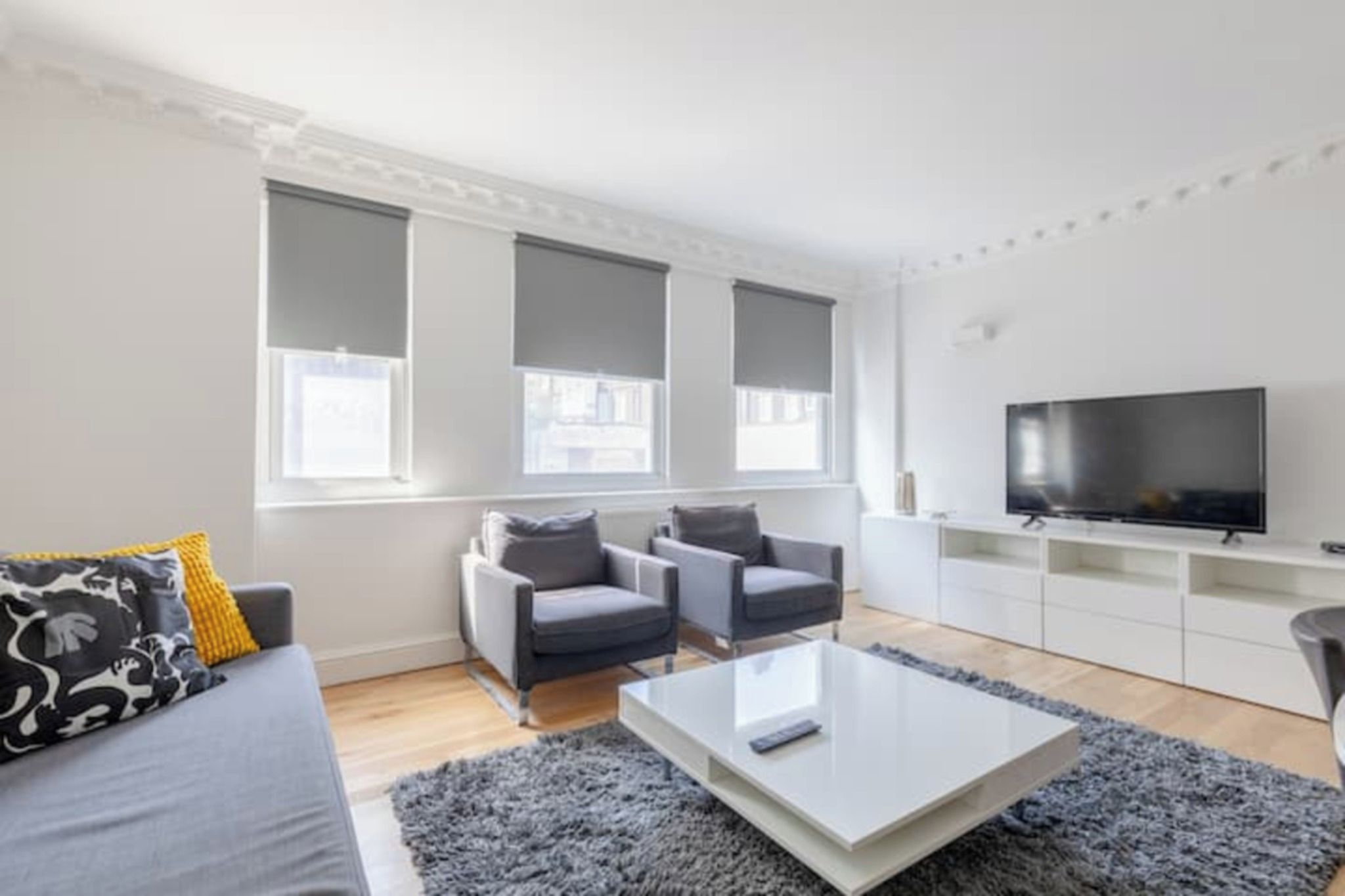 A modern living room with a sofa, two armchairs, a coffee table, and a TV.