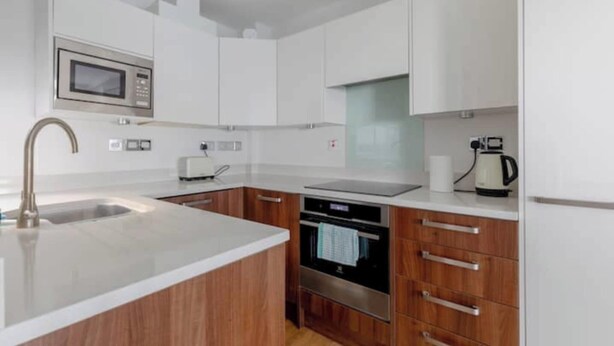 A modern kitchen with white cabinetry, a stainless steel microwave, an oven, and a coffee maker. - Central 2BD Flat, 10 Mins to Buckingham Palace! (London)