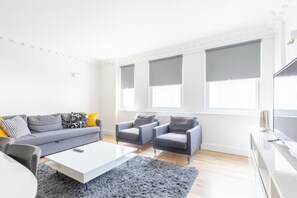 A modern living room with a grey sofa, two armchairs, a white coffee table, and a grey rug.