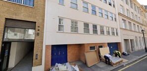 A multi-story residential building with a garage door, a blue door, and a staircase leading to the entrance.