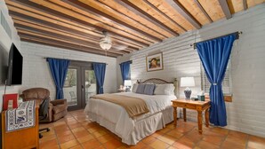 Un dormitorio con cama, escritorio, silla, televisor y ventana con cortinas.