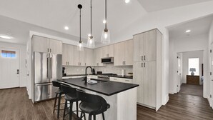 Een moderne keuken met roestvrijstalen apparatuur, een centraal eiland met barstoelen en hanglampen.