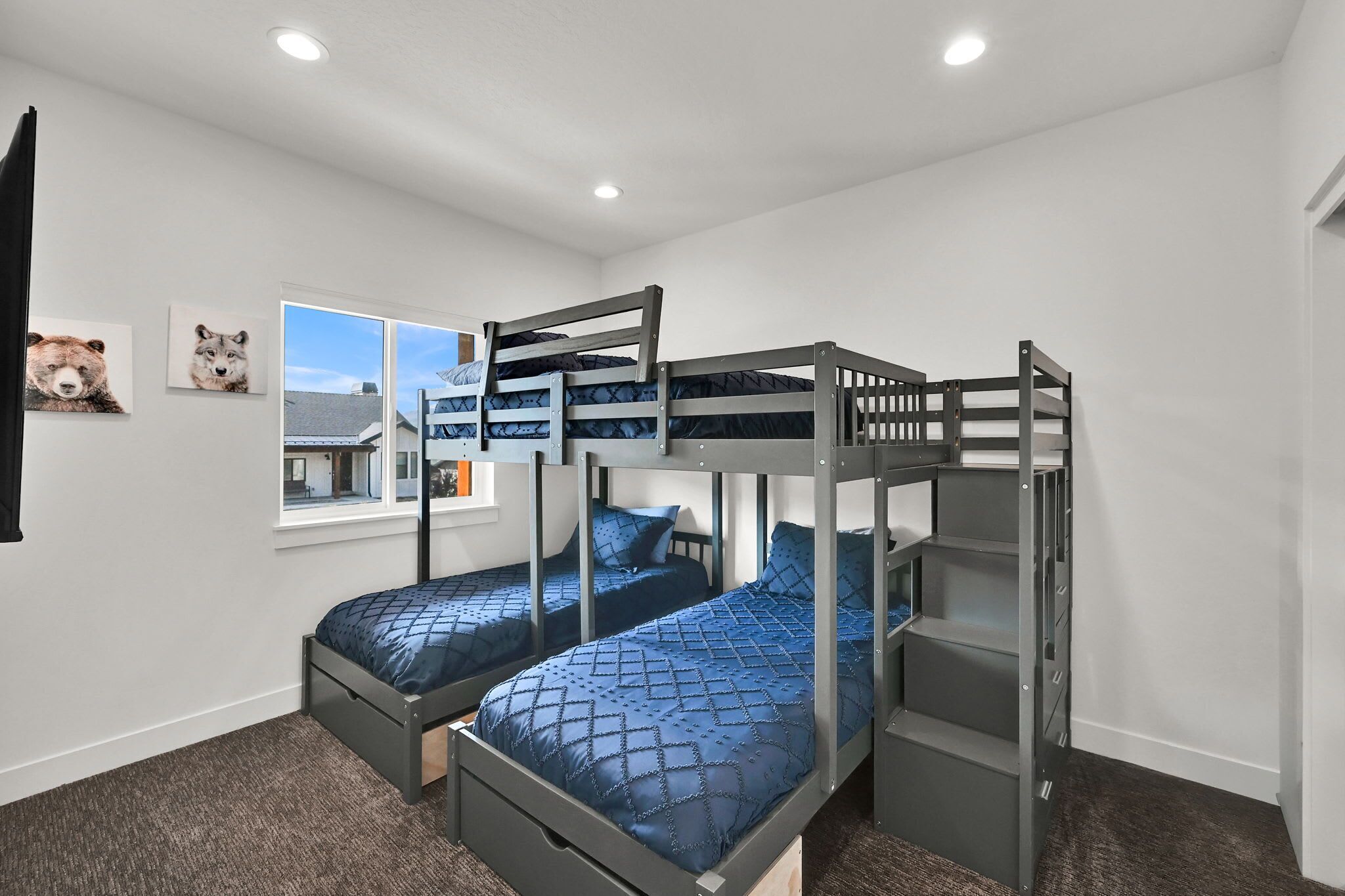 A bunk bed room with a window view, a bear picture on the wall, and a small desk.