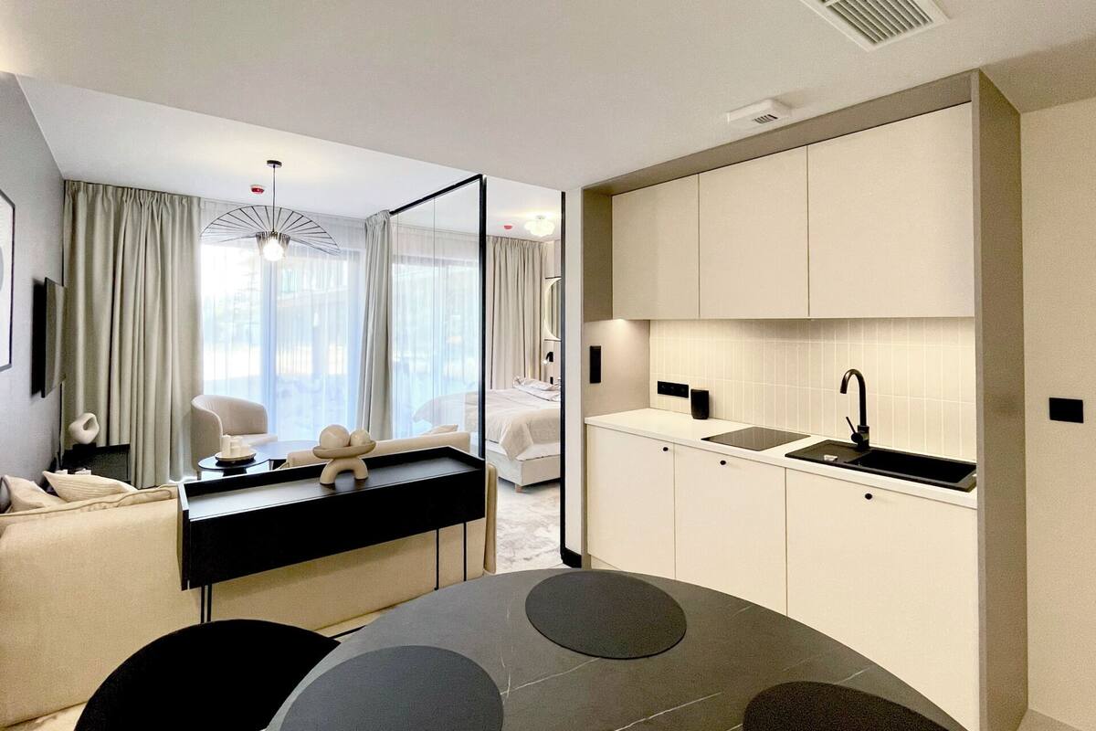 Habitación de hotel moderna con comedor, kitchenette y un amplio ventanal con cortinas.
