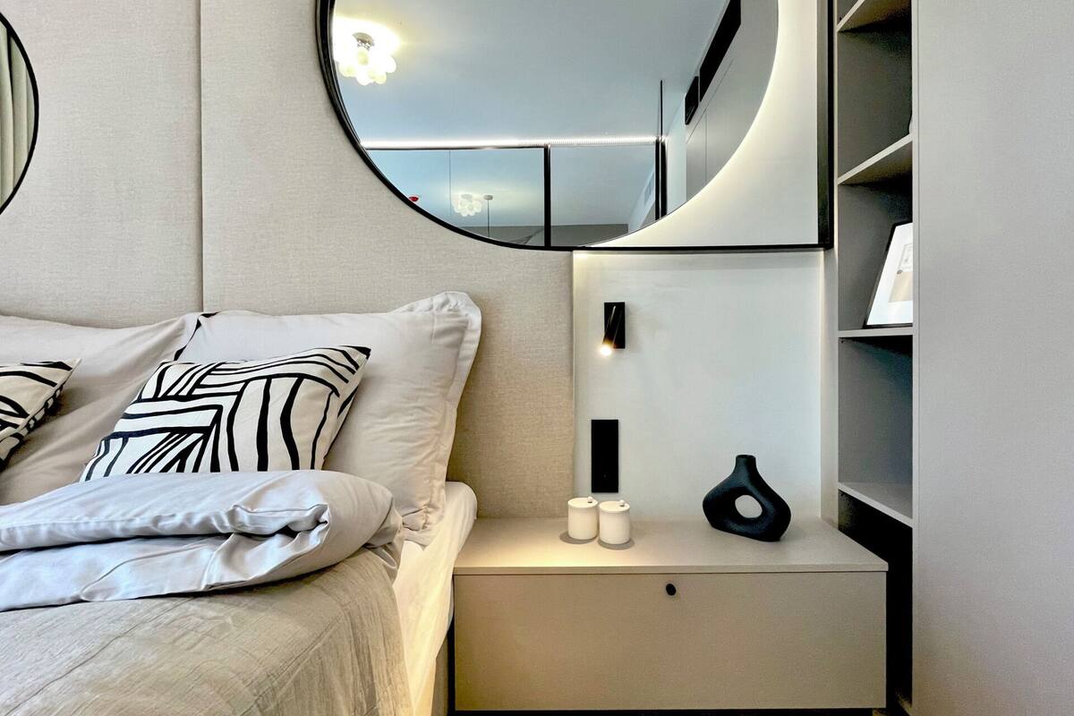 Un dormitorio moderno con cama, mesitas de noche, un espejo y una mesilla.