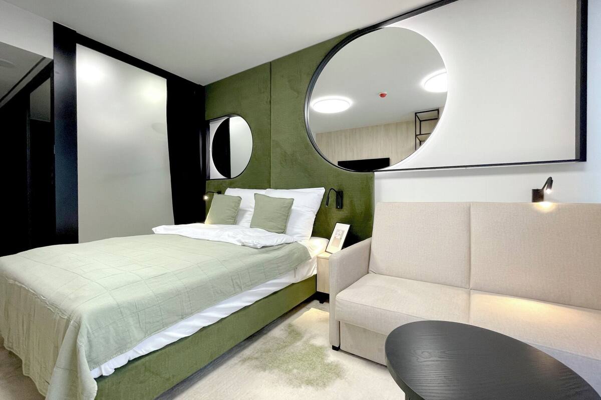 Un dormitorio moderno con una cama, un espejo redondo, un sofá y una mesita.