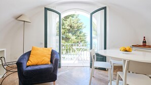 A room with a dark blue sofa, a yellow pillow, a white table with a bowl of lemons, and a balcony with a tree view. - Casa Alessandra in Anacapri (Anacapri)