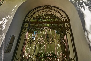 A wrought iron gate with intricate designs, a white wall, and a window with greenery behind it. - Casa Alessandra in Anacapri (Anacapri)