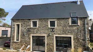 Un edificio de piedra con techo oscuro, varias ventanas y un amplio ventanal corredera.