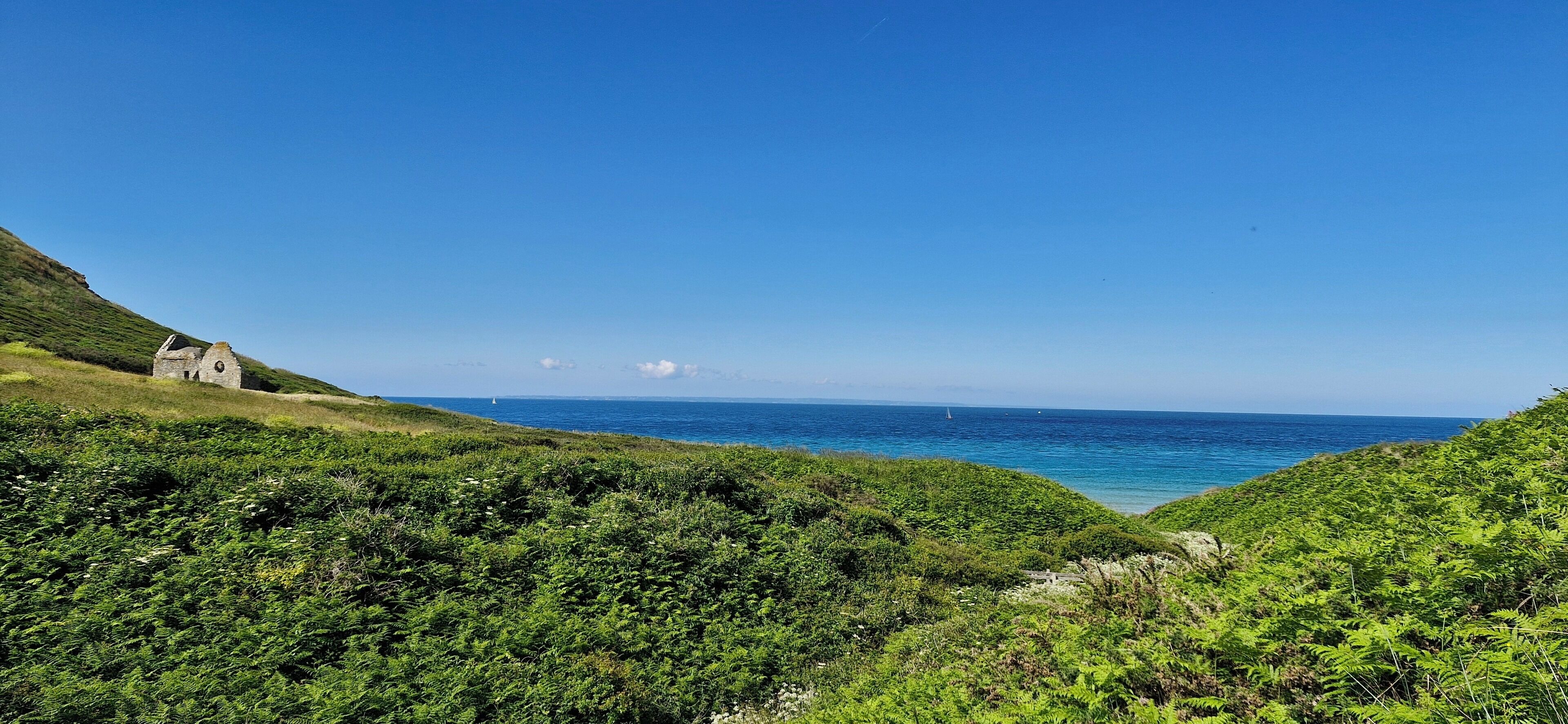 Un paysage côtier avec un petit bâtiment en pierre, une végétation luxuriante et la mer.