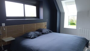Un dormitorio con una cama, una mesita de noche, una lámpara y dos ventanas.
