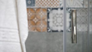 Un bagno con porta doccia in vetro e parete rivestita di piastrelle con diversi motivi.