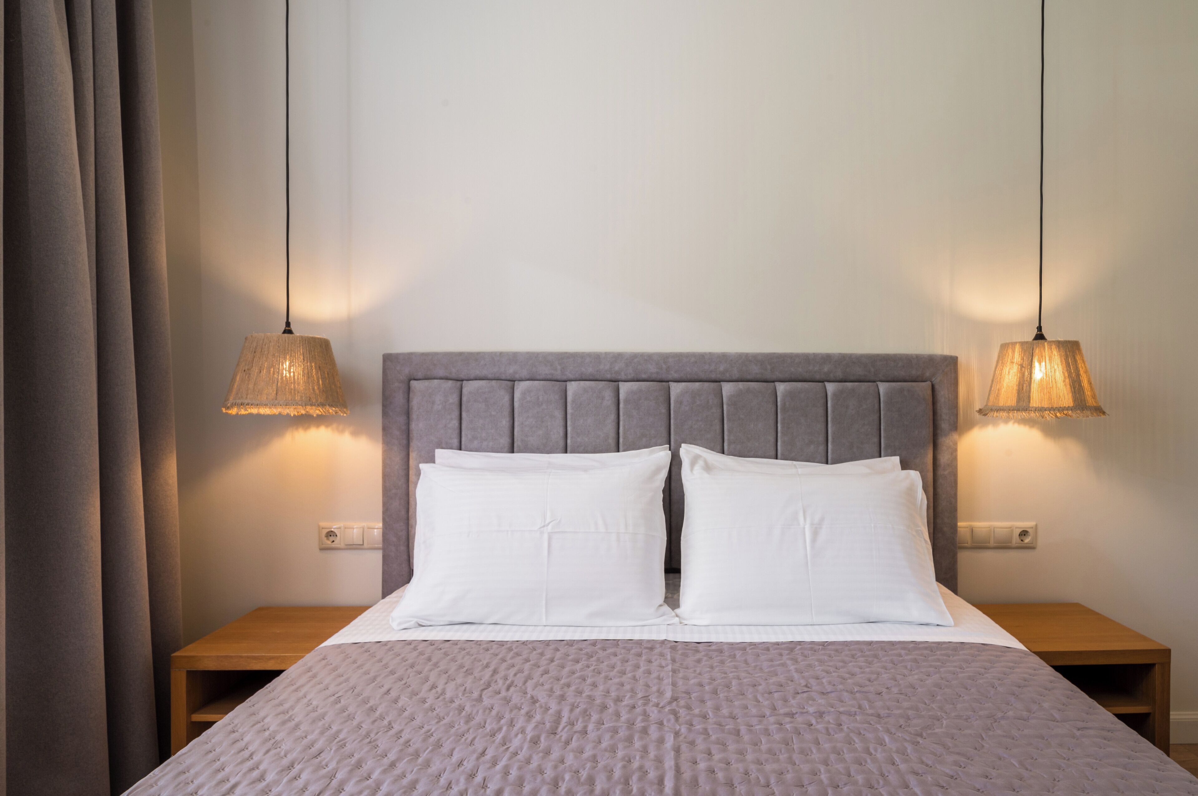 A neatly made bed with a grey headboard, two bedside lamps, and a wooden nightstand.