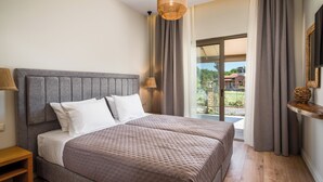 A double bed with a grey headboard, two bedside lamps, and a view of a garden through a sliding glass door. - Phos Elegant Residences by Konnect, 400m to the beach (Corfu)