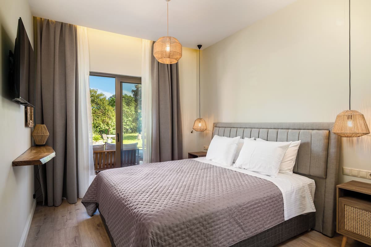 A bedroom with a large bed, a TV mounted on the wall, and a view of the outdoors through a sliding door.