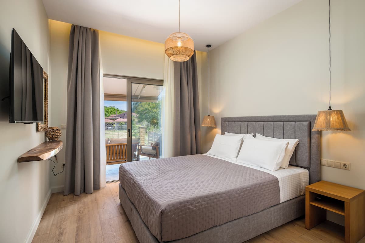 A bedroom with a large bed, a TV mounted on the wall, a wooden nightstand, and a view of the outdoors through a sliding glass door.