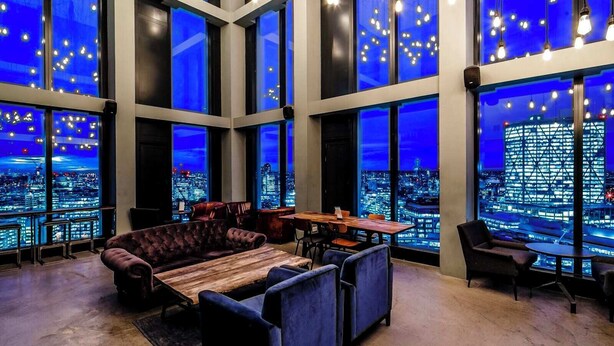 Un amplio salón con grandes ventanales que ofrecen vista a la ciudad, iluminación moderna y asientos cómodos.