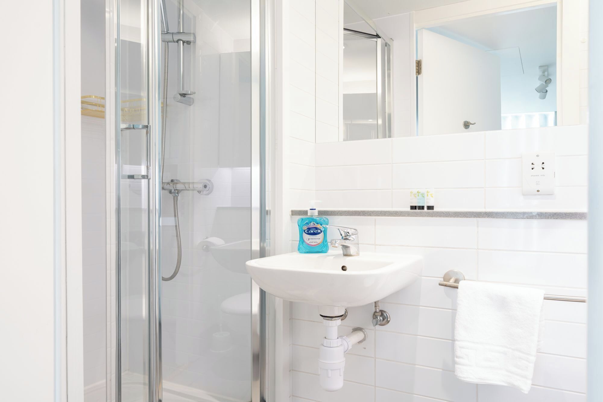 A bathroom with a glass shower enclosure, a white sink, and a mirror above the sink.