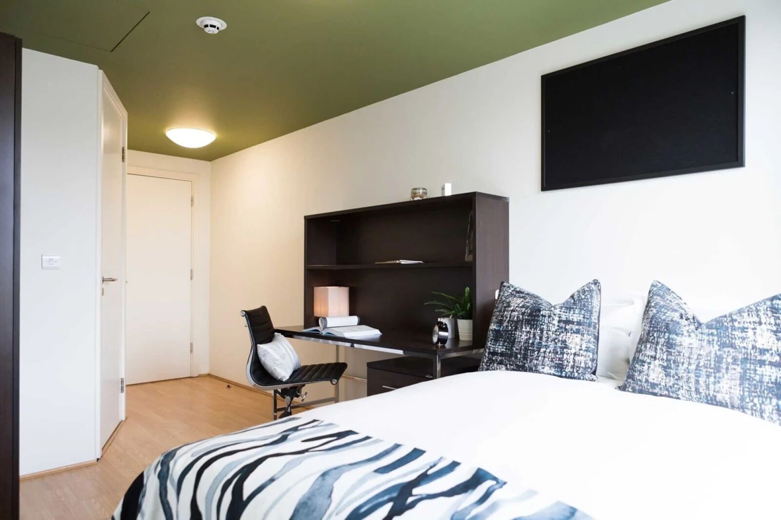 A bedroom with a bed, a desk, a chair, a bookshelf, and a door.