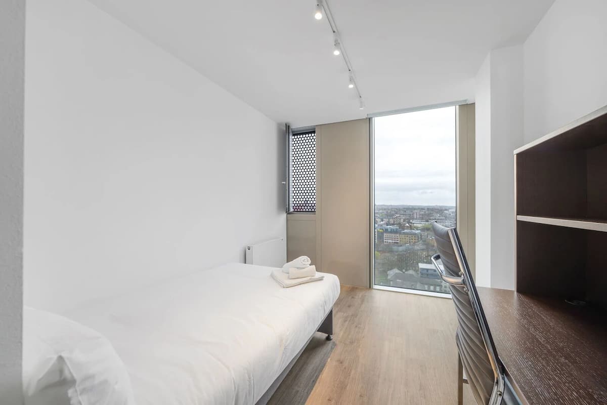Ein modernes Hotelzimmer mit großem Fenster, einem Bett, einem Kleiderschrank und Blick auf die Stadt.