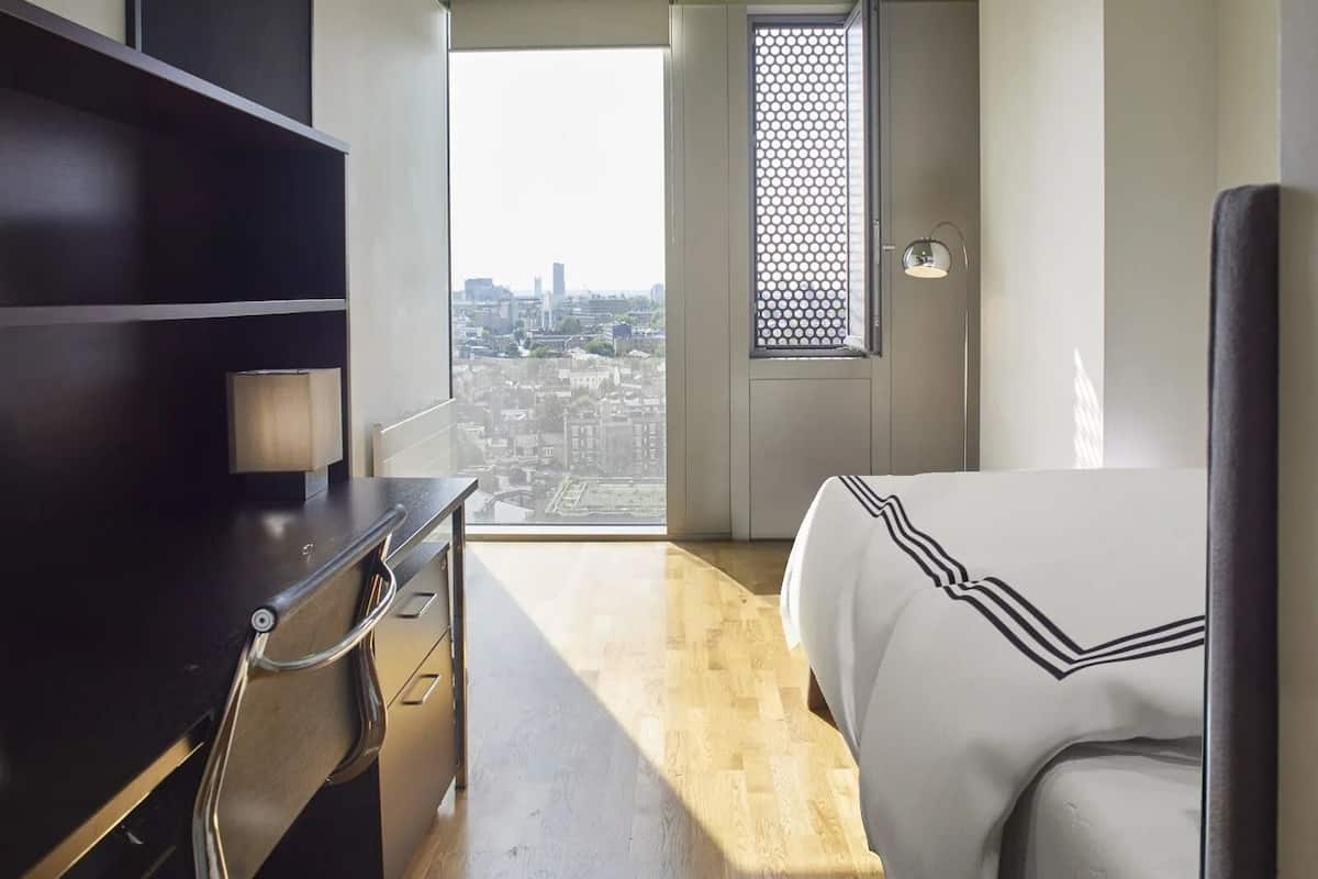 Ein Hotelzimmer mit Bett, Schreibtisch und Blick auf die Stadt durch ein Fenster.