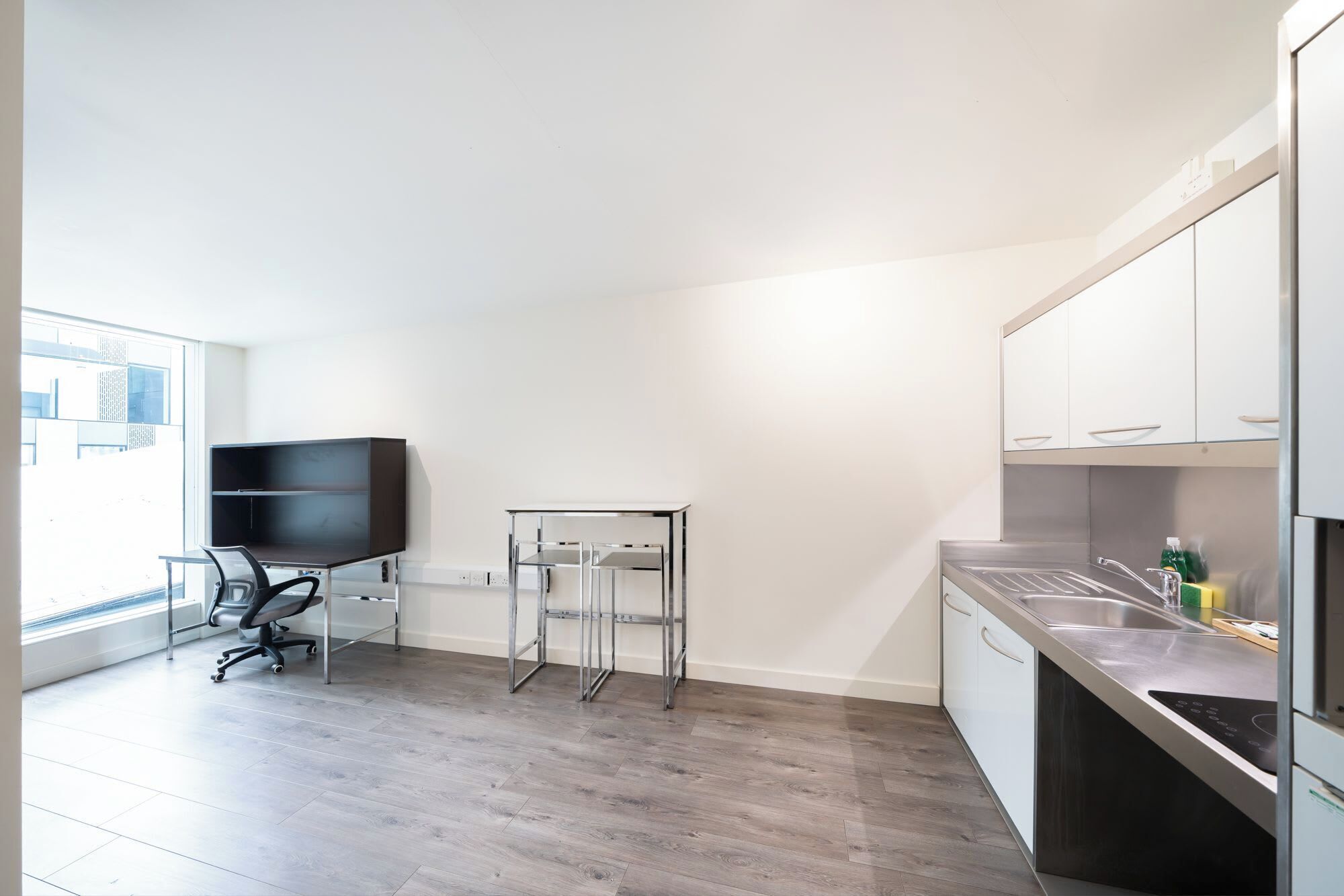 A modern kitchen with a built-in stove, a sink, and a dining area with a chair and a small table.