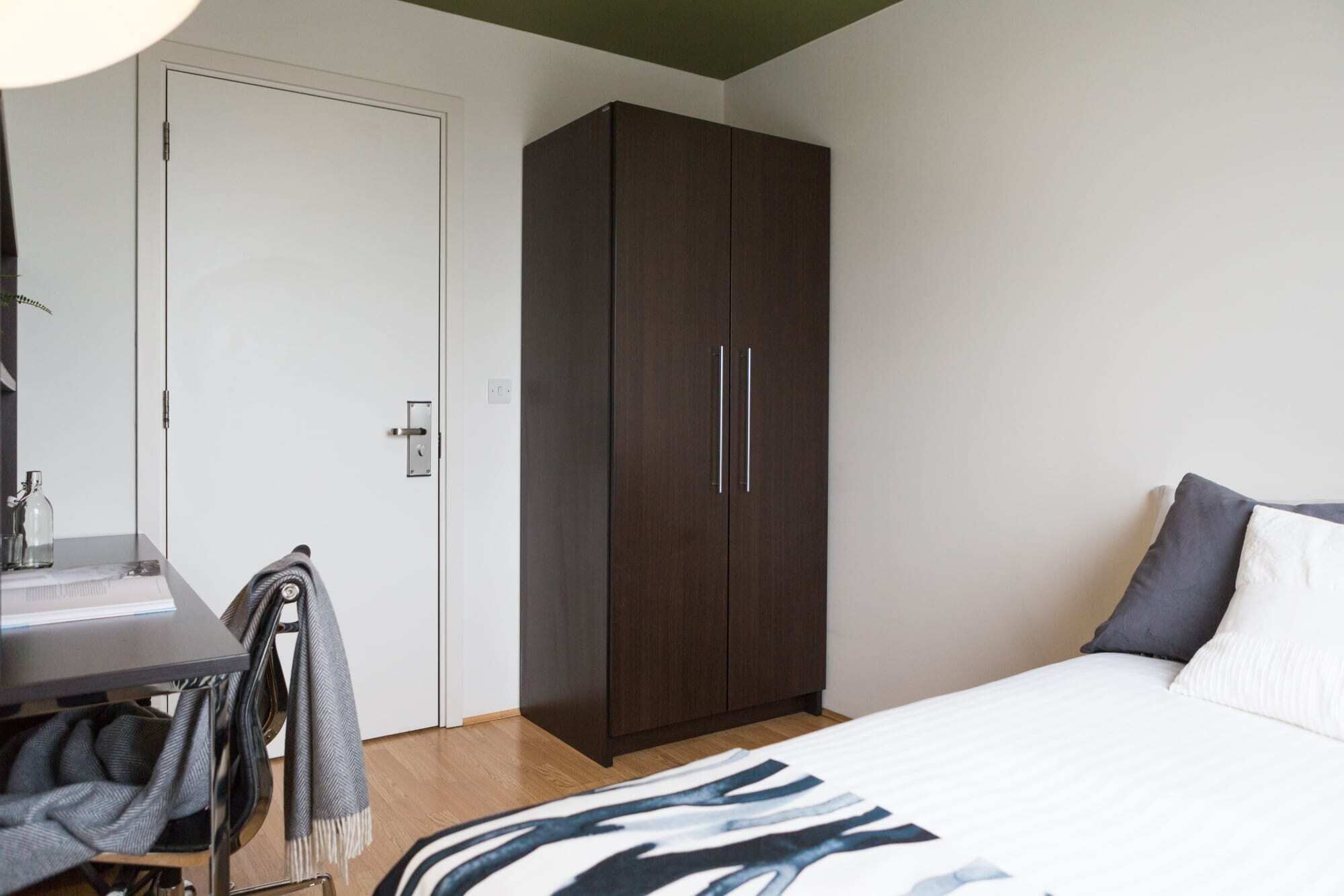 Een slaapkamer met een bed, een kledingkast, een bureau met een lamp en een stoel.